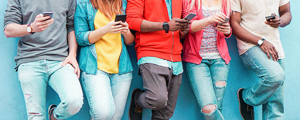 Teenagers texting mobile phone messages leaning on wall